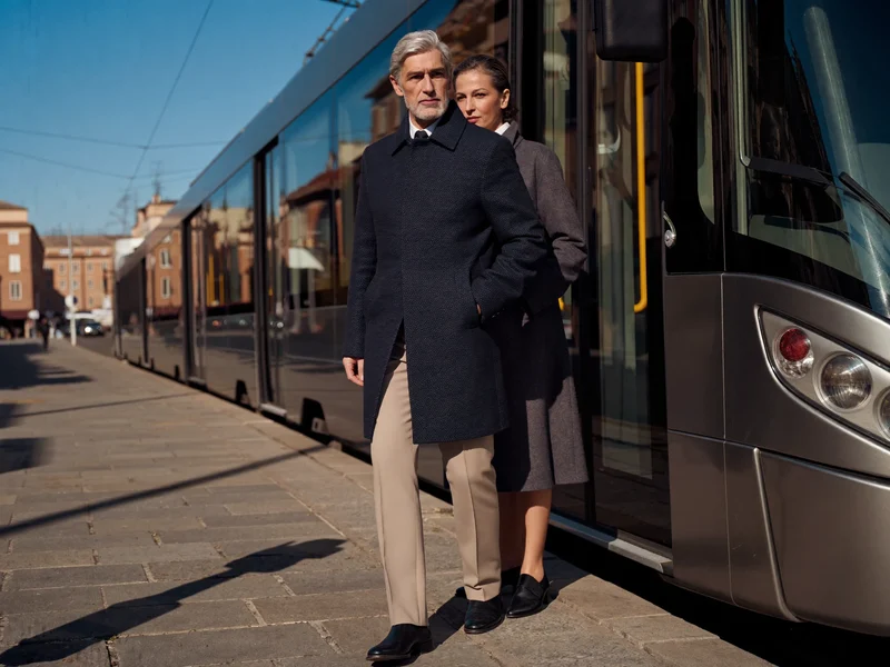 Una coppia di anziani sale su un tram cittadino in una strada soleggiata.